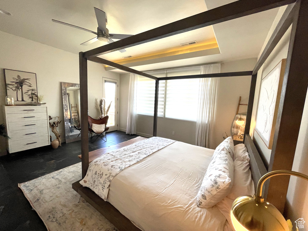 Bedroom with a raised ceiling, multiple windows, ceiling fan, and dark wood-type flooring