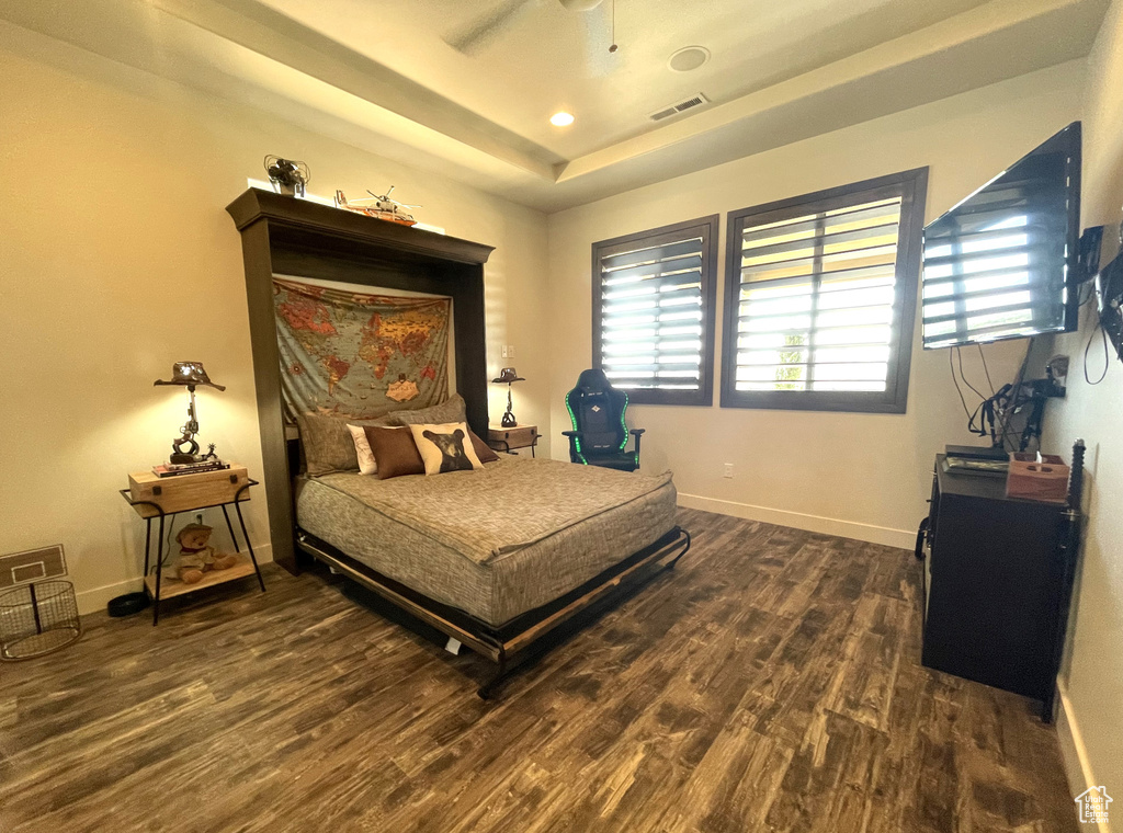 Bedroom featuring dark hardwood / wood-style flooring, ceiling fan, and a tray ceiling