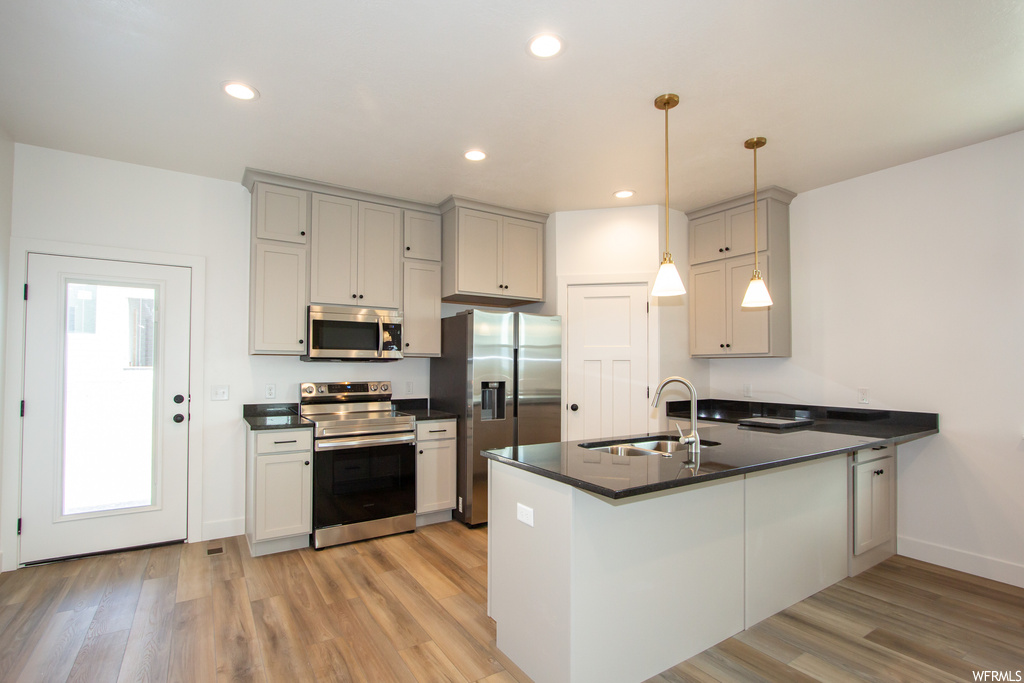 Kitchen featuring kitchen peninsula, light wood-type flooring, pendant lighting, and stainless steel appliances