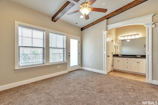 Unfurnished bedroom featuring light colored carpet, ceiling fan, ensuite bath, and multiple windows