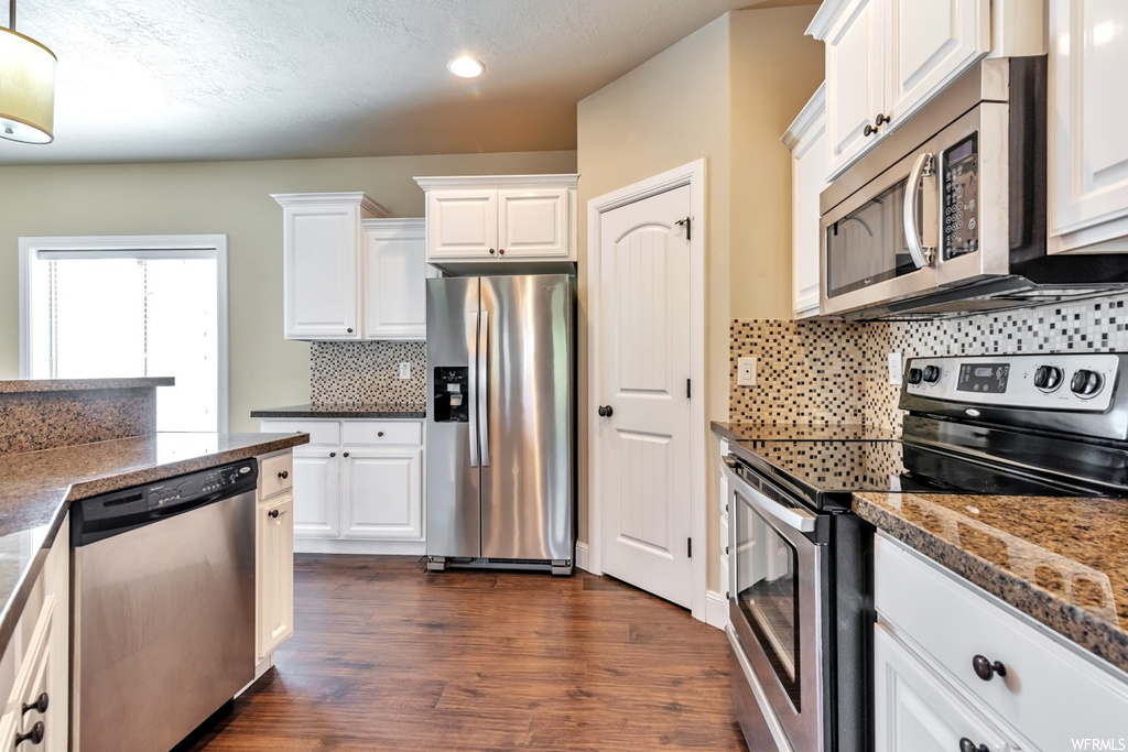 Kitchen with tasteful backsplash, dark hardwood / wood-style floors, stainless steel appliances, and white cabinets