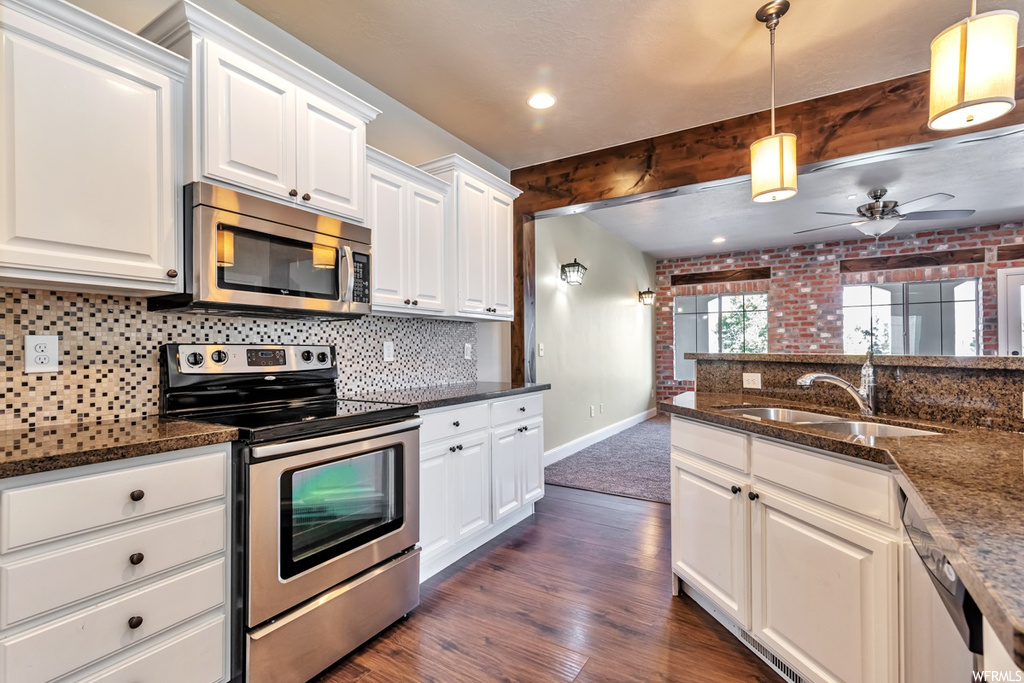 Kitchen with appliances with stainless steel finishes, pendant lighting, ceiling fan, brick wall, and white cabinetry