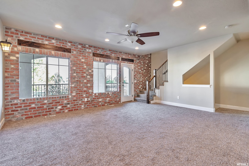 Unfurnished living room featuring ceiling fan, carpet flooring, and brick wall