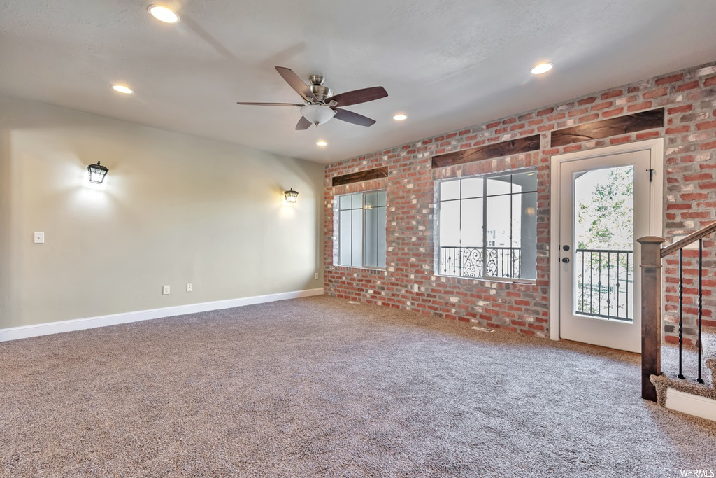 Unfurnished room with ceiling fan, brick wall, and carpet
