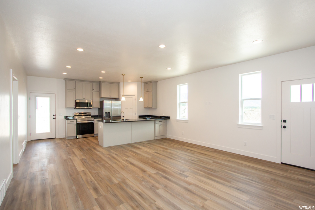 Kitchen featuring hanging light fixtures, kitchen peninsula, light hardwood / wood-style flooring, and stainless steel appliances