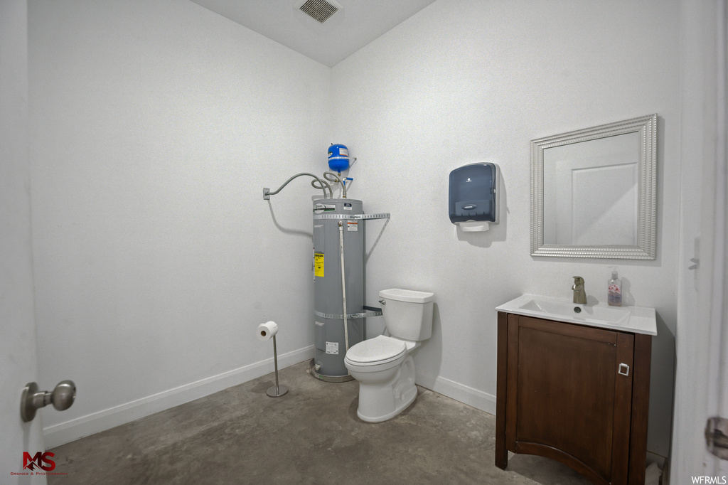 Bathroom featuring toilet, vanity with extensive cabinet space, strapped water heater, and concrete flooring