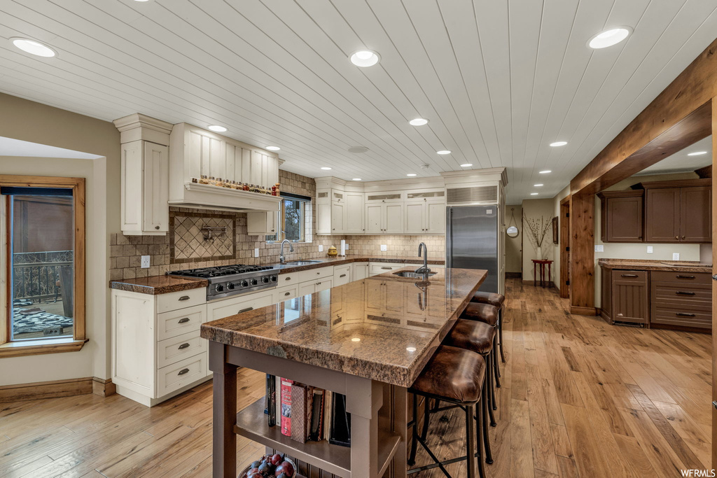 Kitchen featuring dark stone countertops, light wood-type flooring, a kitchen bar, and appliances with stainless steel finishes