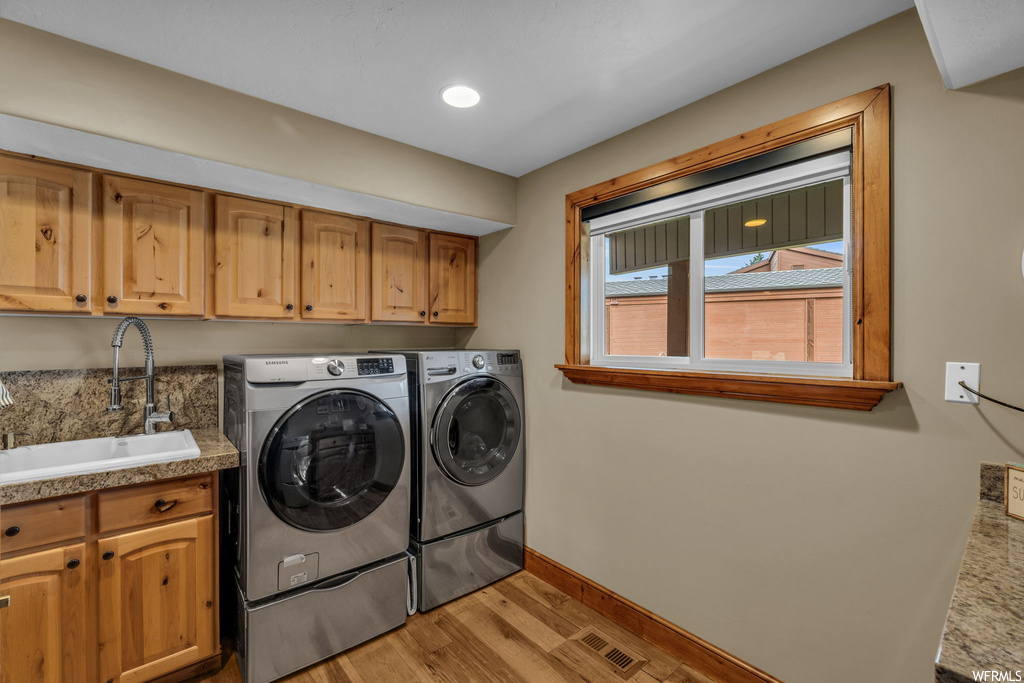 Clothes washing area with washer and clothes dryer, cabinets, sink, and light hardwood / wood-style floors
