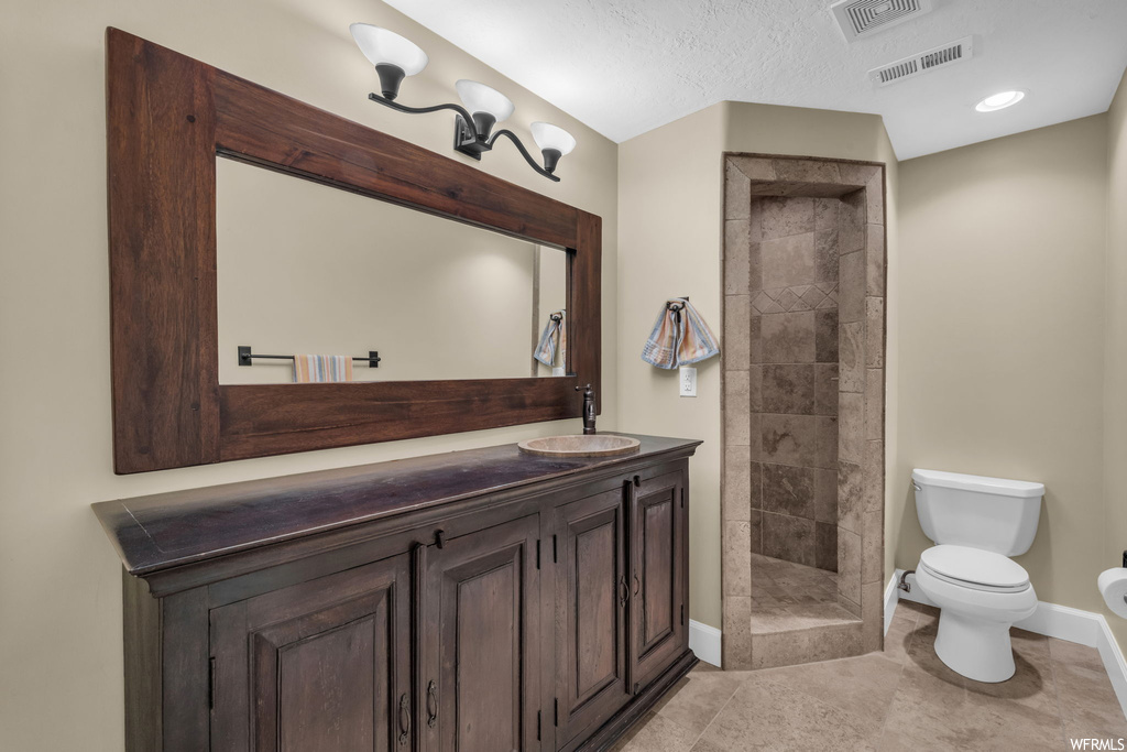 Bathroom with toilet, a textured ceiling, tile flooring, tiled shower, and vanity