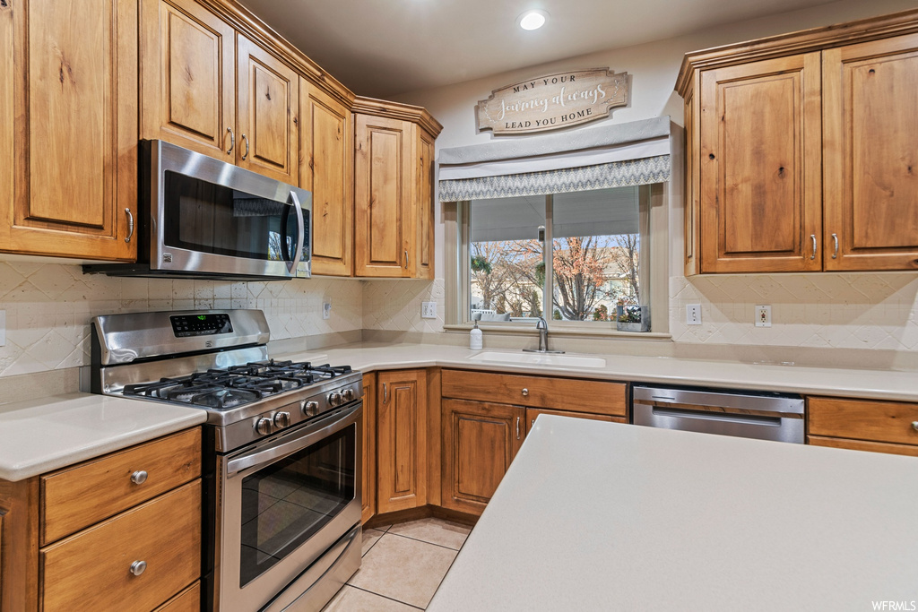 Kitchen with backsplash, light tile floors, sink, and appliances with stainless steel finishes