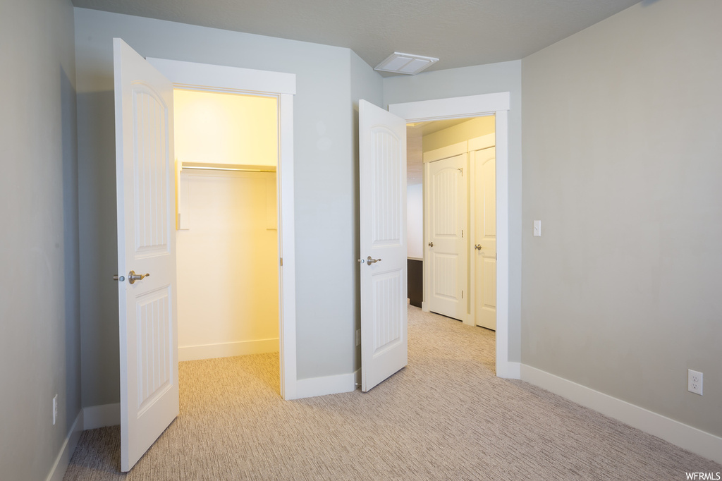 Unfurnished bedroom featuring a spacious closet, a closet, and light carpet
