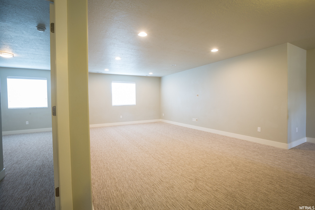 Empty room with light colored carpet, a textured ceiling, and a wealth of natural light