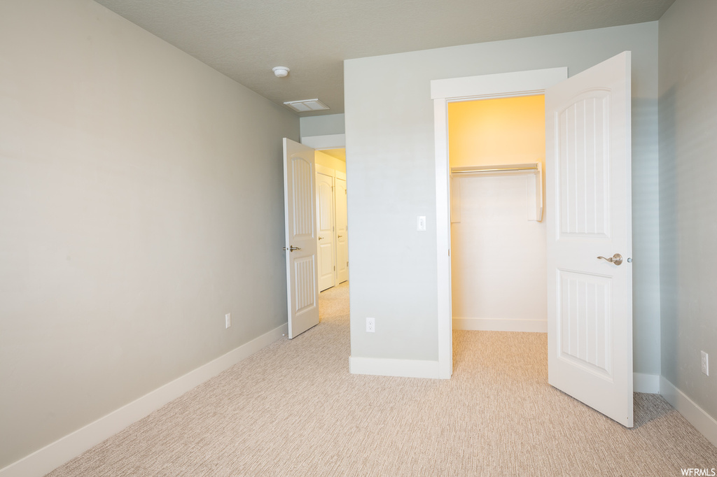 Unfurnished bedroom featuring a spacious closet, a closet, and light colored carpet