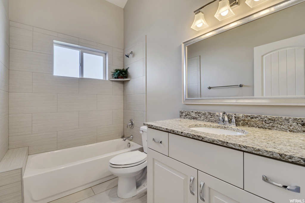 Full bathroom featuring toilet, tile floors, large vanity, and tiled shower / bath