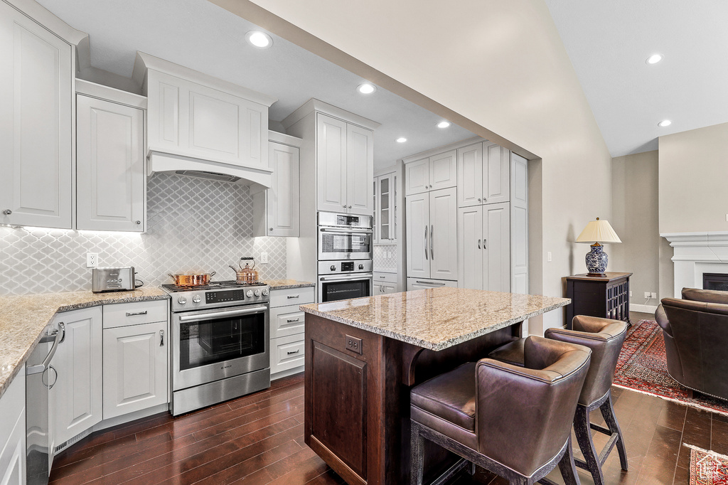 Kitchen featuring tasteful backsplash, appliances with stainless steel finishes, dark wood-type flooring, and white cabinetry