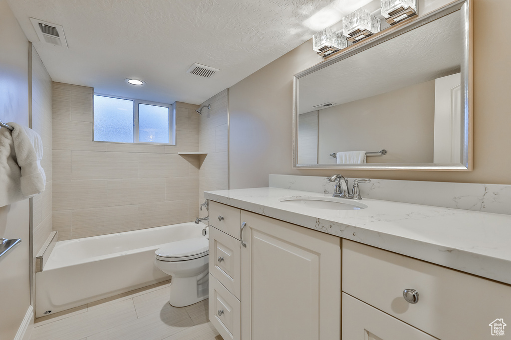 Full bathroom with tiled shower / bath, tile floors, vanity, toilet, and a textured ceiling