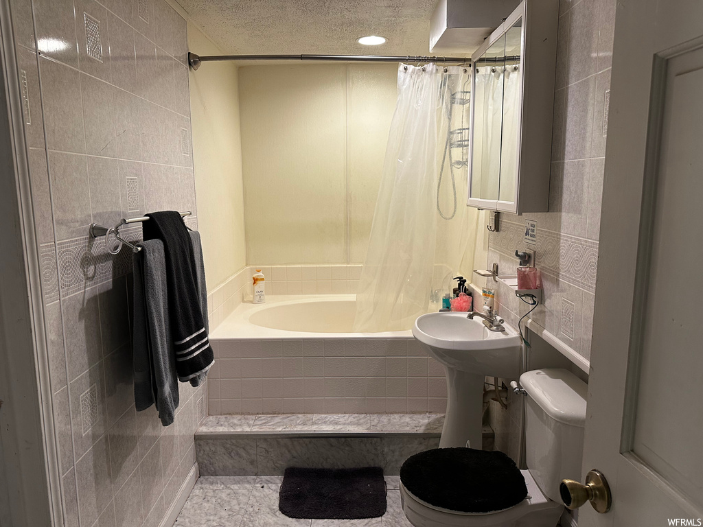 Full bathroom with sink, shower / bath combo, tile walls, toilet, and a textured ceiling