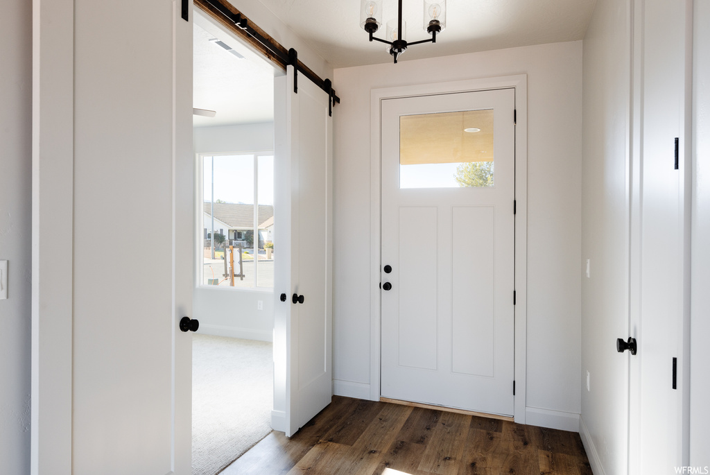 Entryway featuring dark carpet, an inviting chandelier, and a barn door