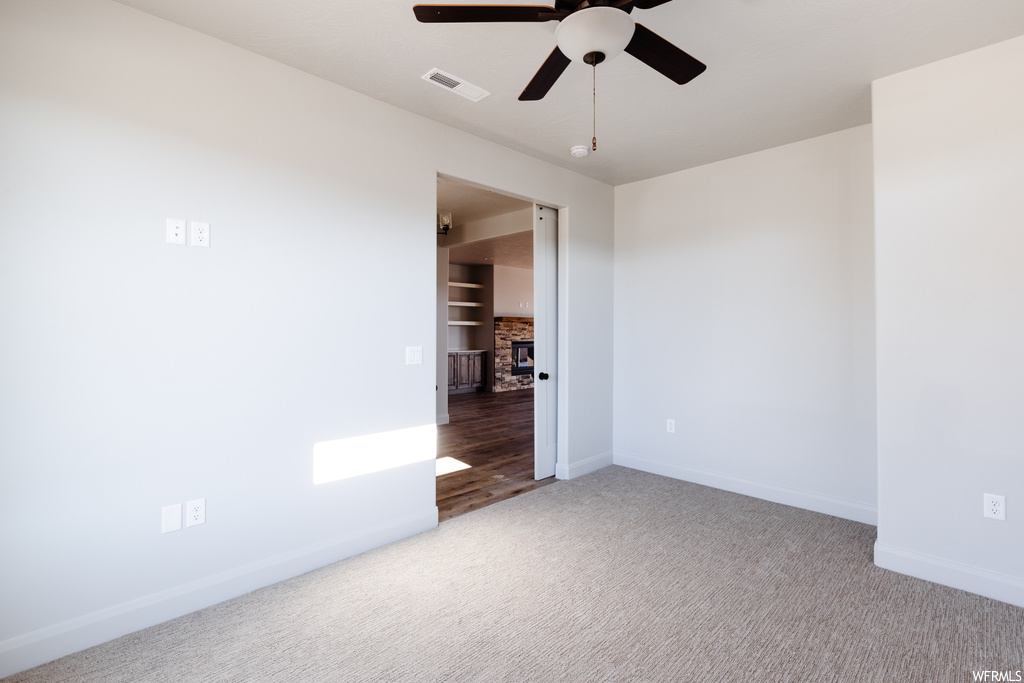 Unfurnished room with ceiling fan, a stone fireplace, and light carpet