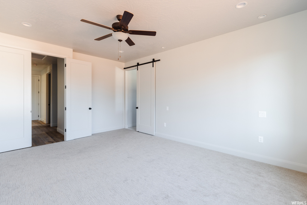 Interior space featuring a barn door, ceiling fan, and light carpet