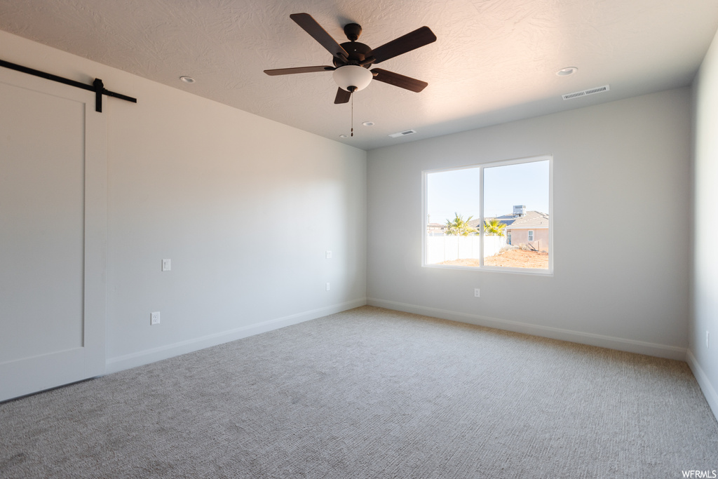 Spare room with a barn door, ceiling fan, and light colored carpet
