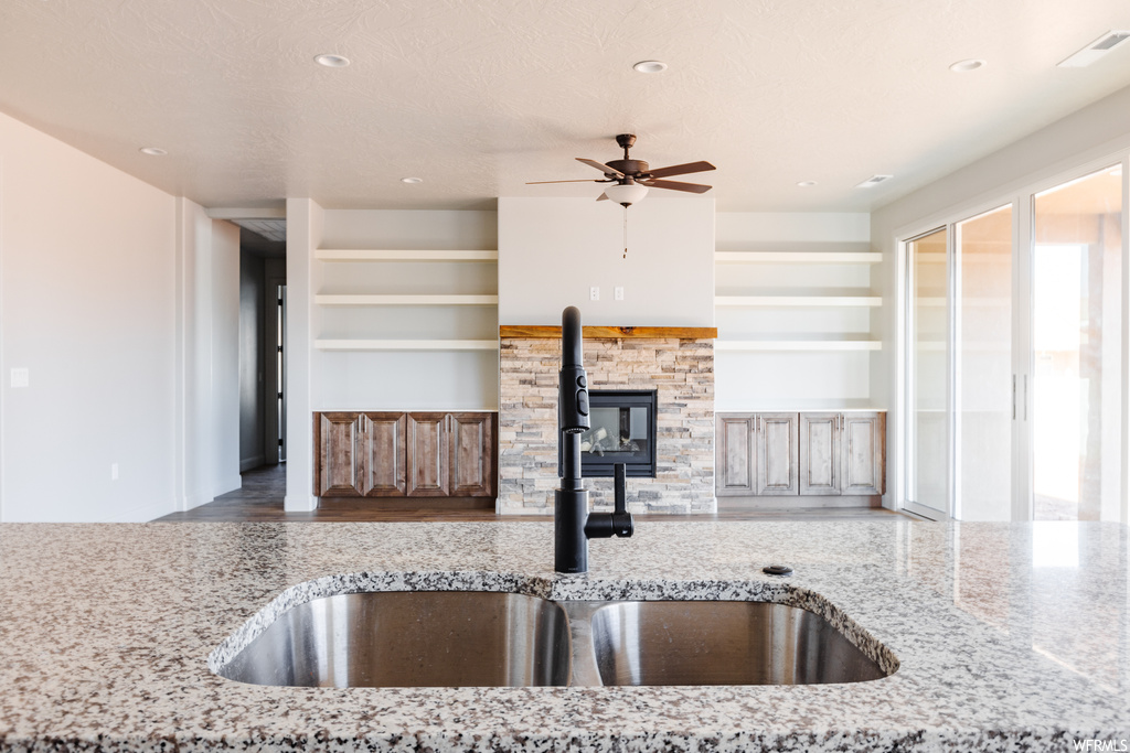 Kitchen with sink, light stone countertops, built in shelves, ceiling fan, and a textured ceiling