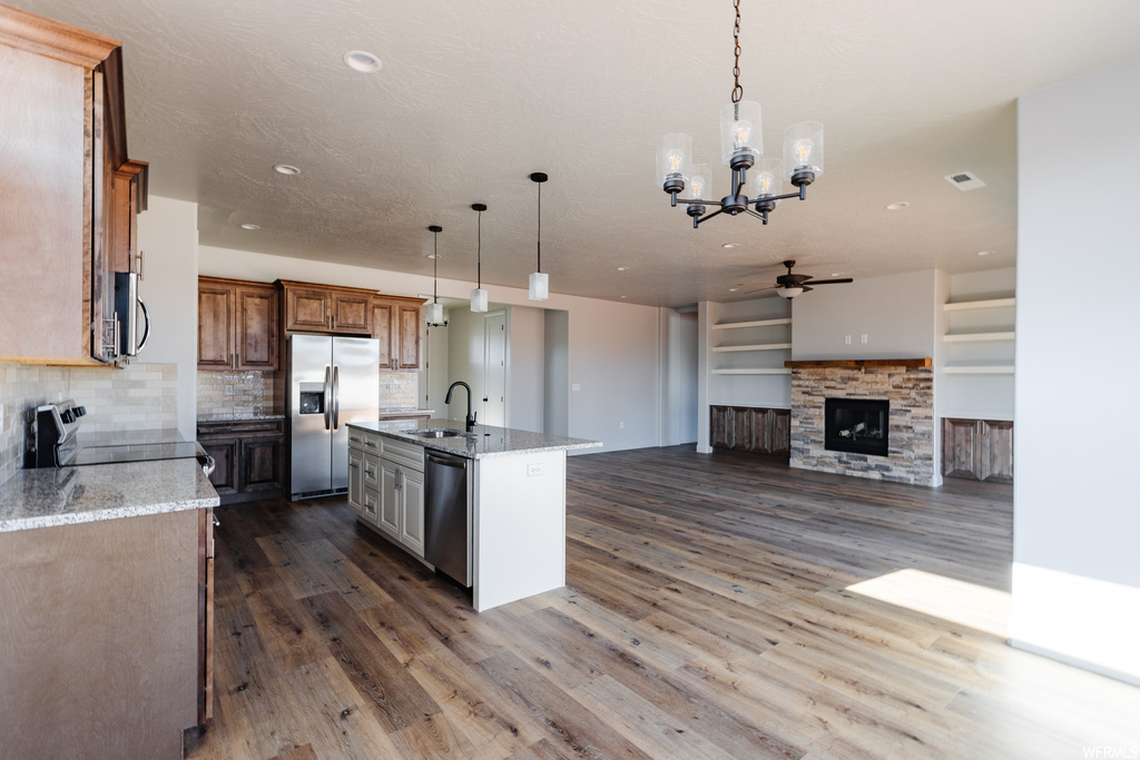 Kitchen with dark wood-type flooring, sink, appliances with stainless steel finishes, a kitchen island with sink, and decorative light fixtures
