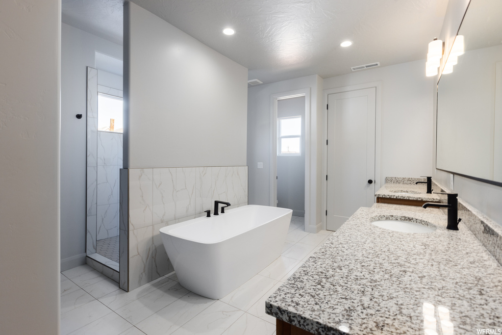 Bathroom featuring tile walls, plus walk in shower, double sink, tile floors, and large vanity