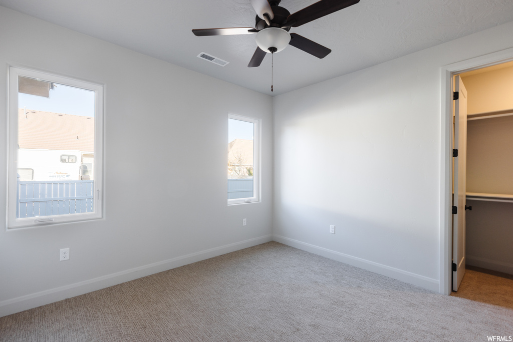 Unfurnished bedroom featuring a closet, light colored carpet, ceiling fan, and a spacious closet