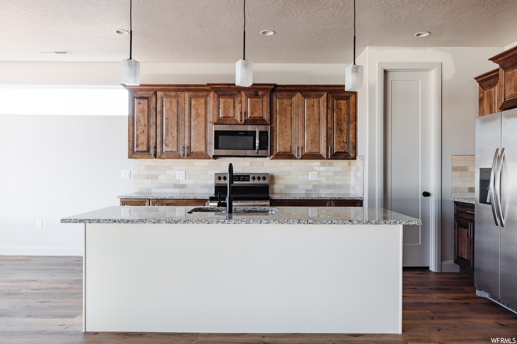 Kitchen featuring pendant lighting, a kitchen island with sink, stainless steel appliances, backsplash, and dark hardwood / wood-style floors