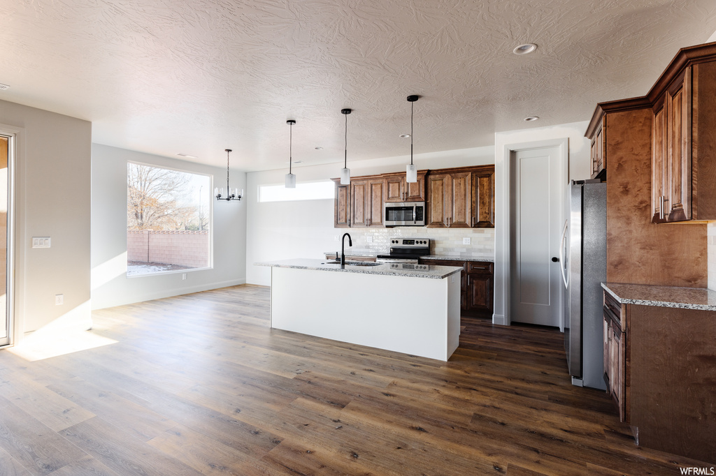 Kitchen featuring an island with sink, hanging light fixtures, dark hardwood / wood-style flooring, and stainless steel appliances