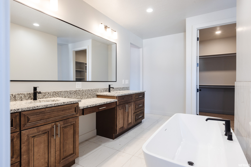 Bathroom with tile floors, vanity with extensive cabinet space, dual sinks, and a bath