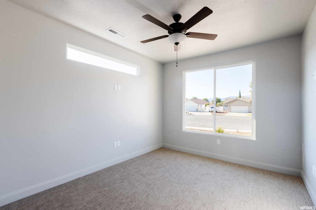Spare room with a healthy amount of sunlight, ceiling fan, and light colored carpet