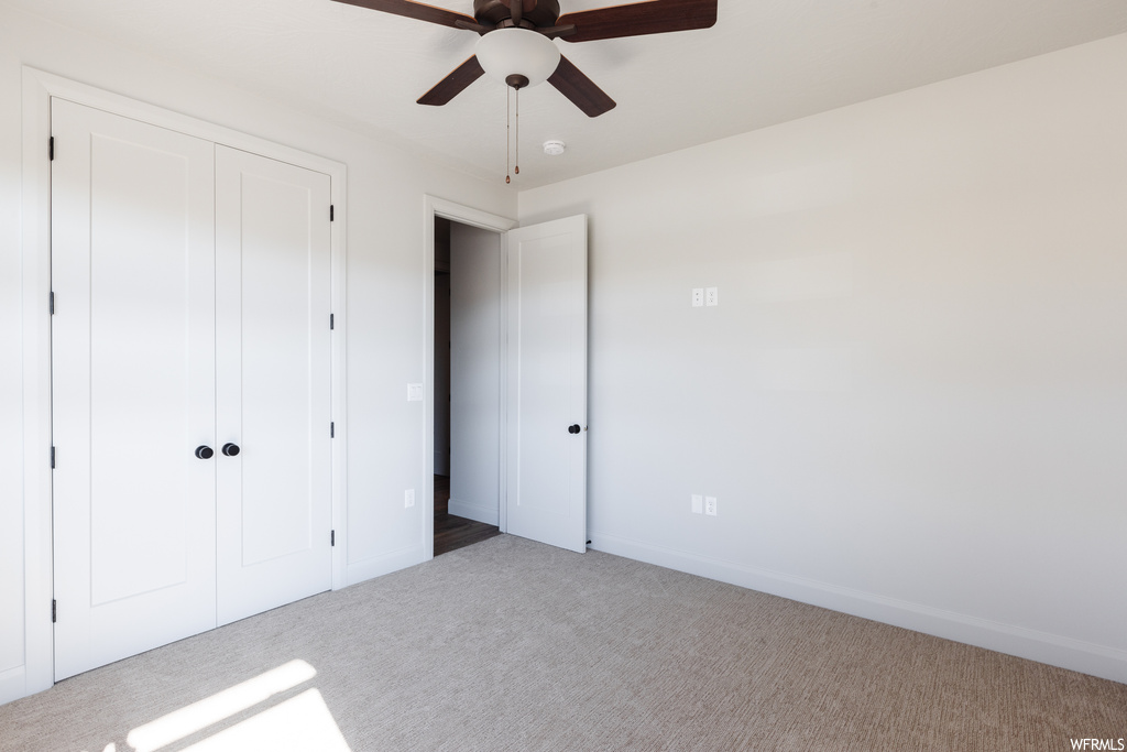 Unfurnished bedroom with ceiling fan, a closet, and light carpet