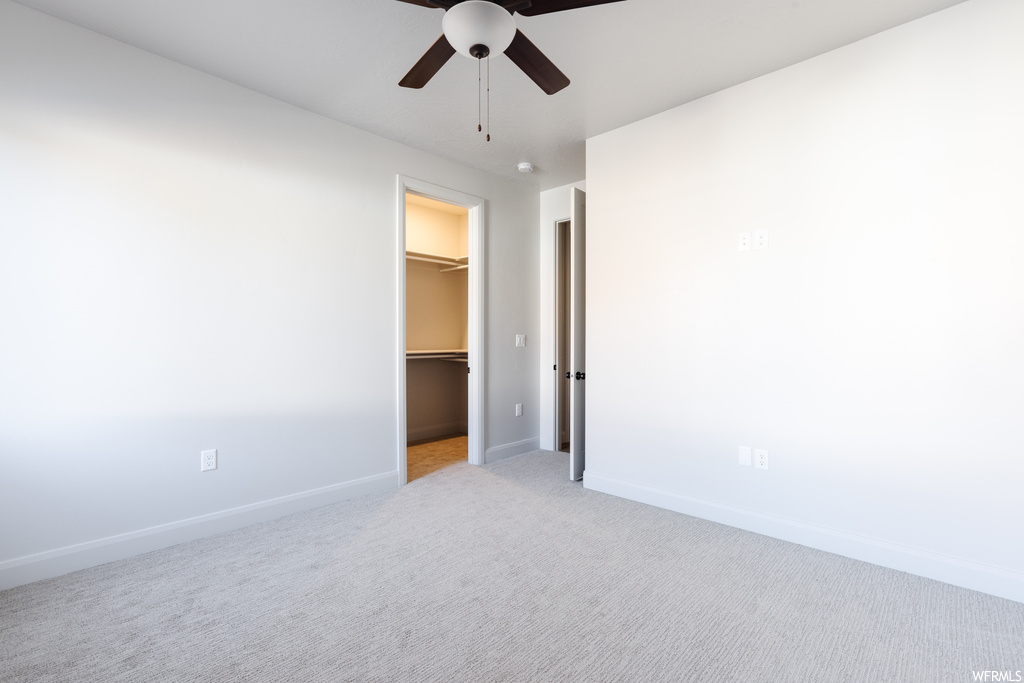 Unfurnished bedroom with a walk in closet, a closet, ceiling fan, and light colored carpet