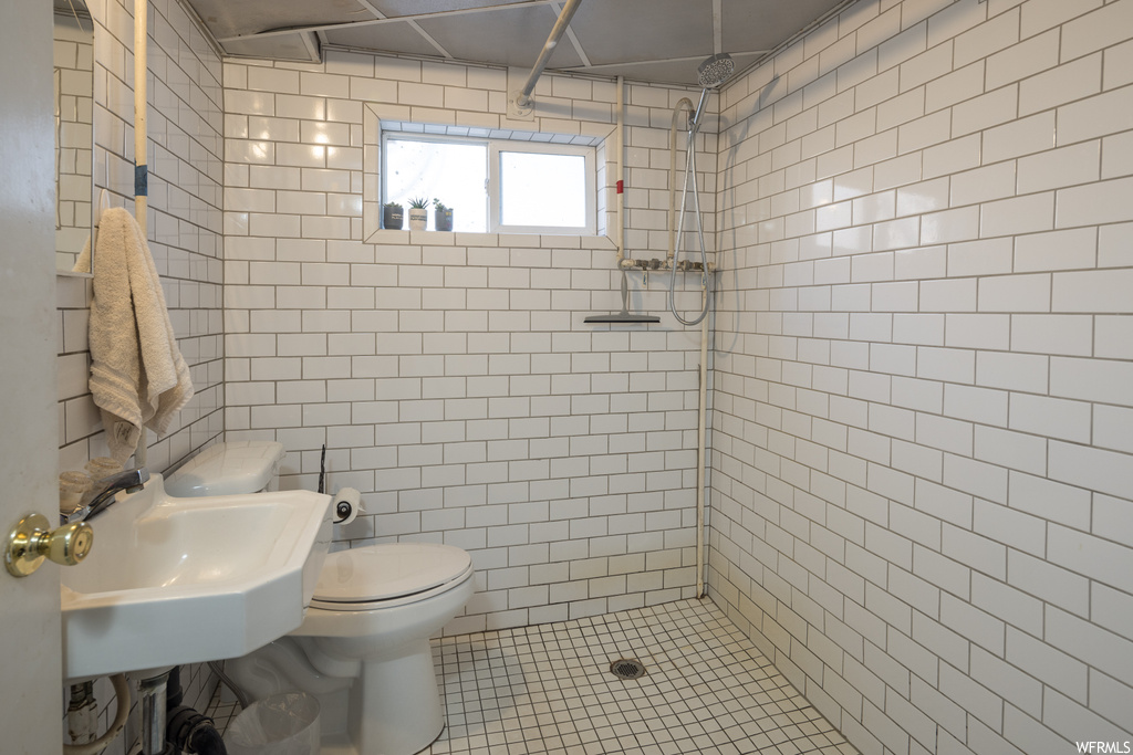Bathroom with toilet, sink, tile walls, a tile shower, and tile flooring