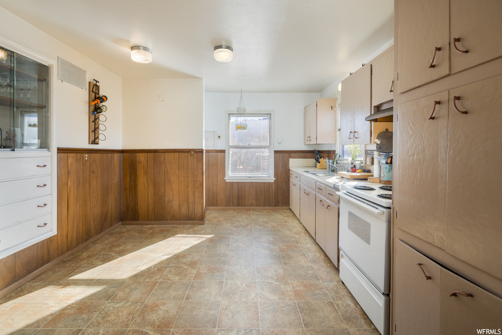 Kitchen featuring light tile floors, wood walls, electric range, and wall chimney exhaust hood