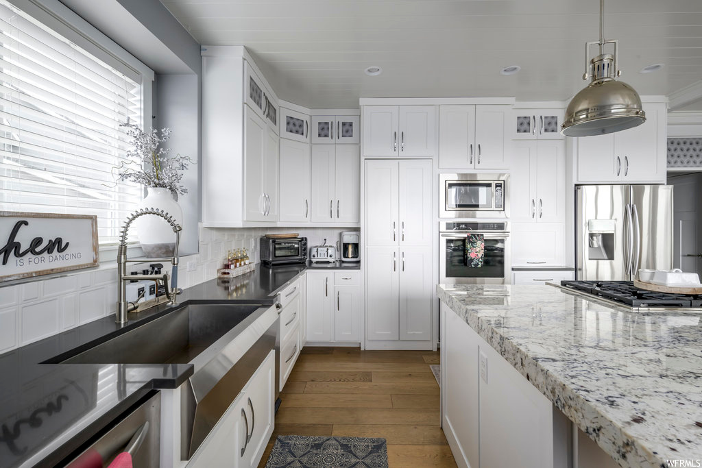 Kitchen featuring light hardwood / wood-style floors, pendant lighting, white cabinetry, backsplash, and stainless steel appliances