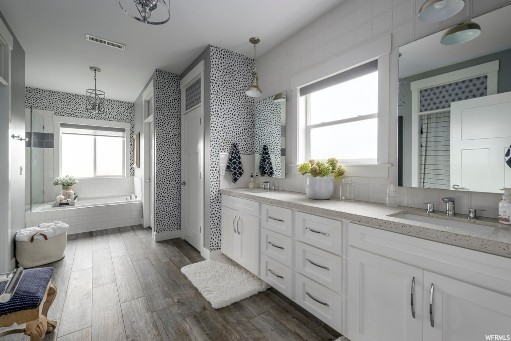 Bathroom featuring double vanity, hardwood / wood-style flooring, backsplash, and tiled tub