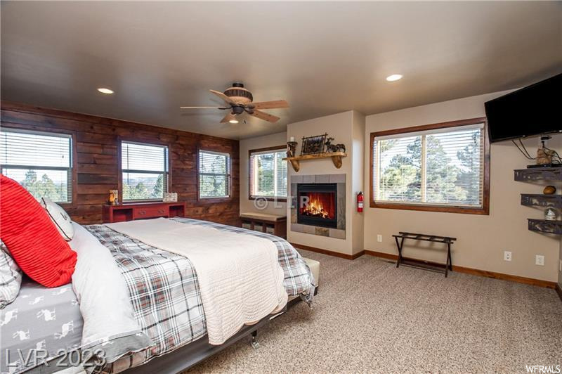 Carpeted bedroom featuring wood walls, ceiling fan, and a fireplace