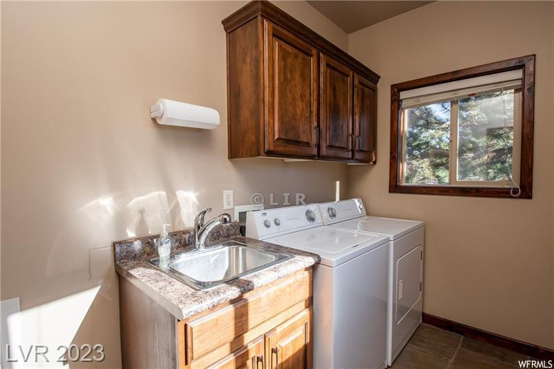 Washroom with washer hookup, cabinets, sink, dark tile floors, and washer and clothes dryer
