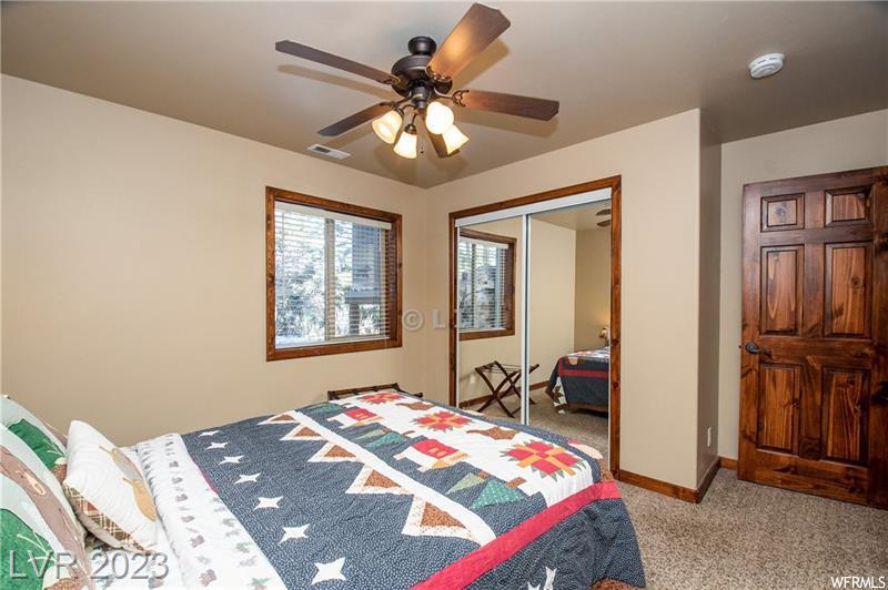 Bedroom with light colored carpet, ceiling fan, and a closet
