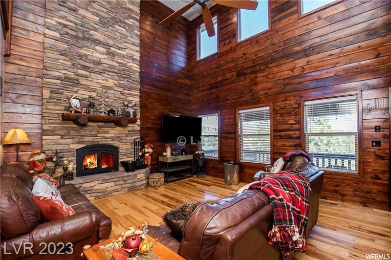 Living room with a fireplace, ceiling fan, a towering ceiling, light hardwood / wood-style flooring, and wooden walls