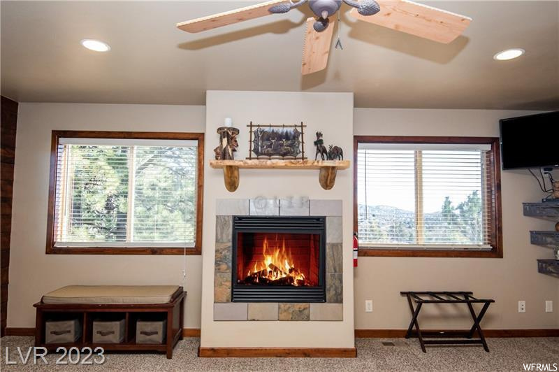 Carpeted living room with a tiled fireplace, ceiling fan, and a healthy amount of sunlight