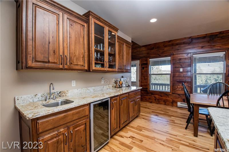 Kitchen featuring sink, wine cooler, light stone counters, wooden walls, and light wood-type flooring