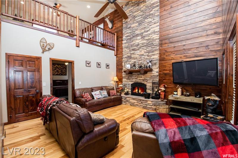 Living room featuring light hardwood / wood-style floors, wooden walls, a high ceiling, ceiling fan, and a stone fireplace