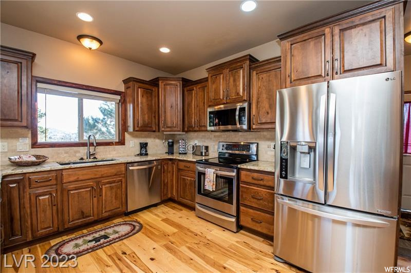 Kitchen featuring sink, light hardwood / wood-style flooring, light stone countertops, stainless steel appliances, and tasteful backsplash