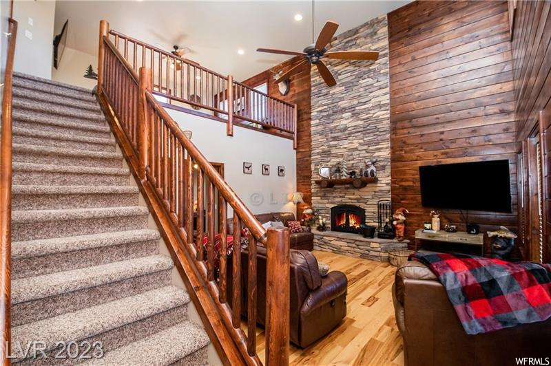 Staircase featuring a stone fireplace, ceiling fan, a high ceiling, light hardwood / wood-style flooring, and wooden walls