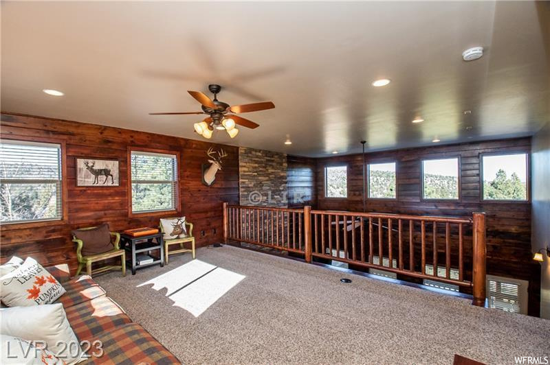 Carpeted living room with ceiling fan and wood walls