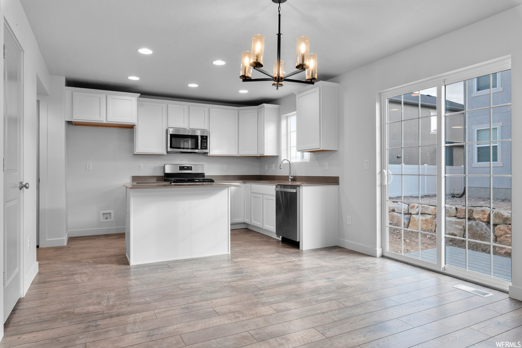 Kitchen with light hardwood / wood-style floors, appliances with stainless steel finishes, decorative light fixtures, a notable chandelier, and white cabinetry